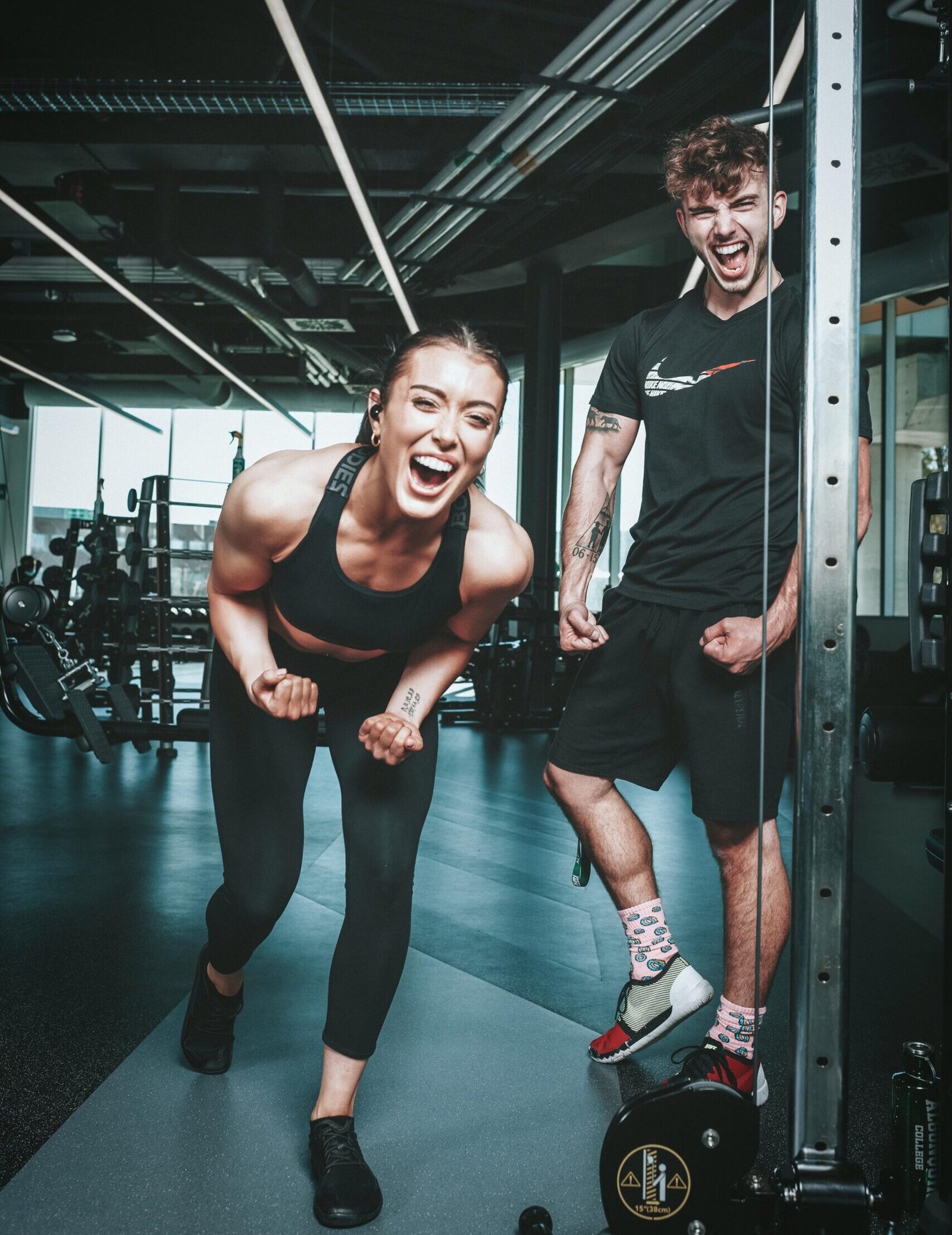 Home Two friends laughing and flexing muscles during a gym workout, embodying a healthy lifestyle.