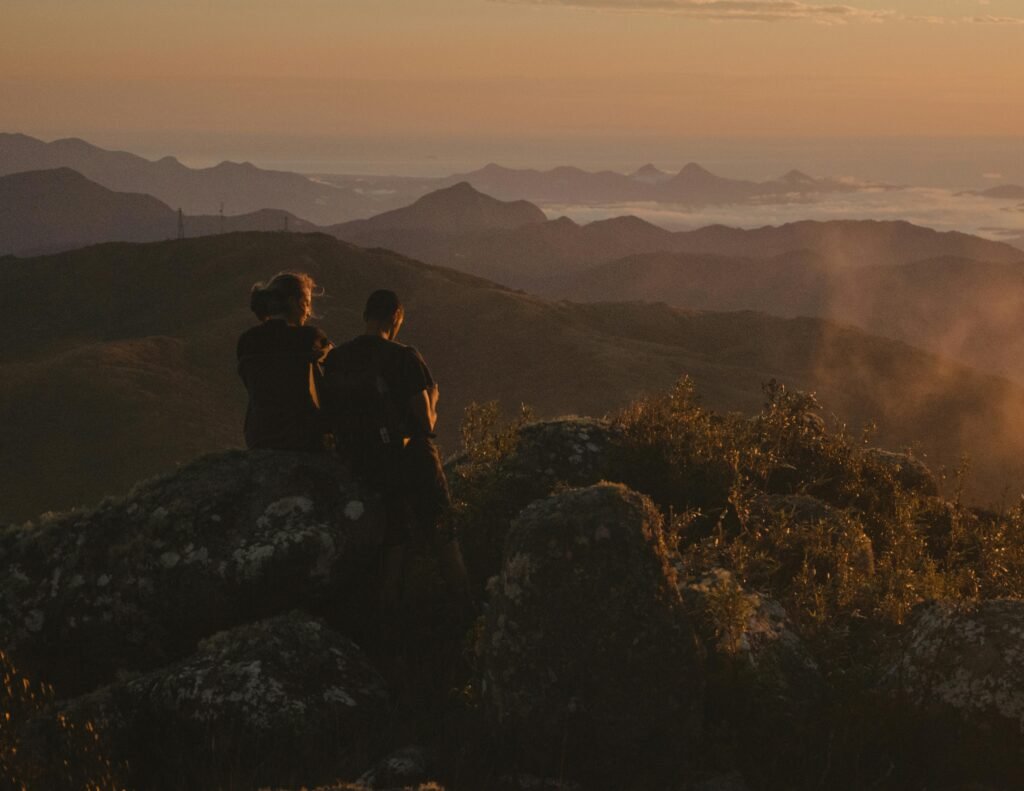 A couple enjoys a serene sunset on a mountain peak, capturing a moment of tranquility.