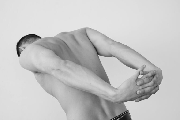 Shirtless man stretching in a black and white studio portrait, showcasing muscle definition.