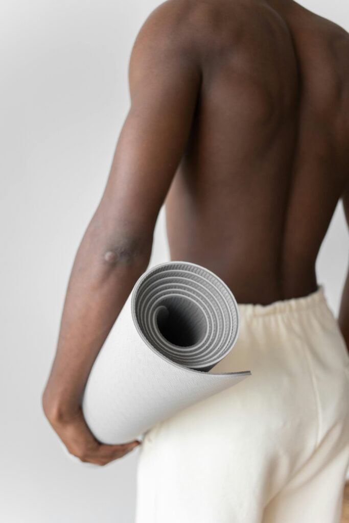 Shirtless man holding a gray yoga mat, promoting a healthy lifestyle.
